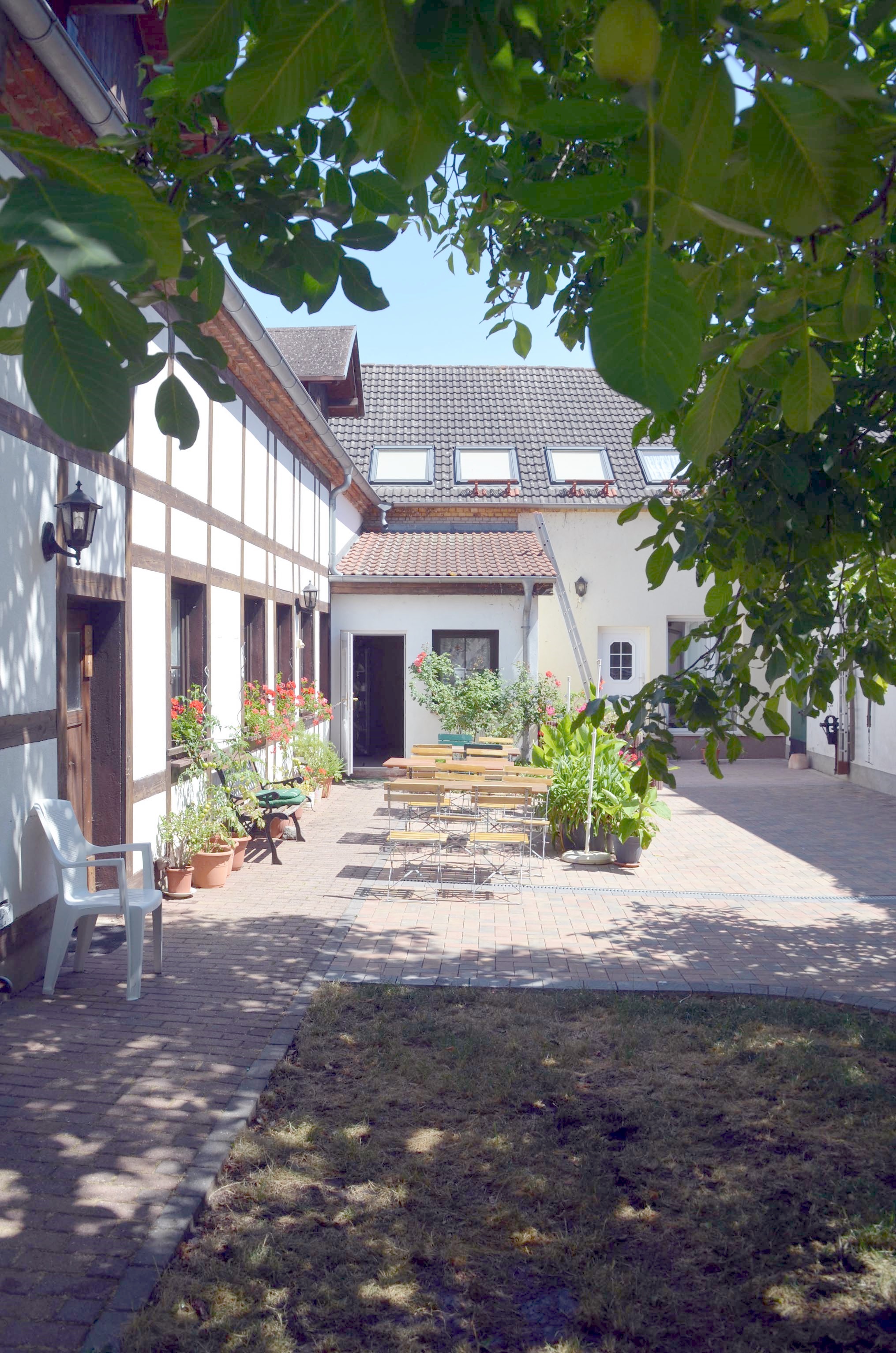 Innenhof der Pension im Sommer: Fachwerkwand mit Geranien, Gartentische unter einem Walnussbaum